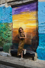 Mature woman checking her smartphone against a colorful mural wall while traveling in Cartagena. Staying connected and travel technology concept. © Gonzalo