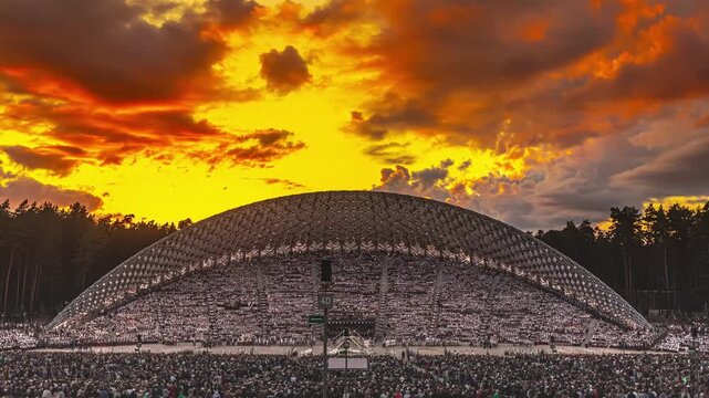 Riga, Latvia - 27 July 2026: View of the Mezaparks Open-Air Stage filled with a large crowd under a vibrant sunset sky.