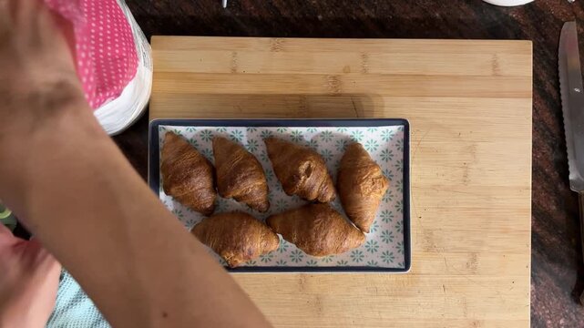 Manos espolvoreando az&uacute;car glass sobre croissants desde cenital