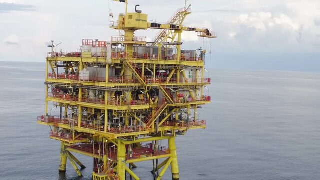 Close-up oblique view of multi-level offshore production platform with suspended crane hook over calm ocean under overcast sky, with offshore, platform, oilrig, rig detail
