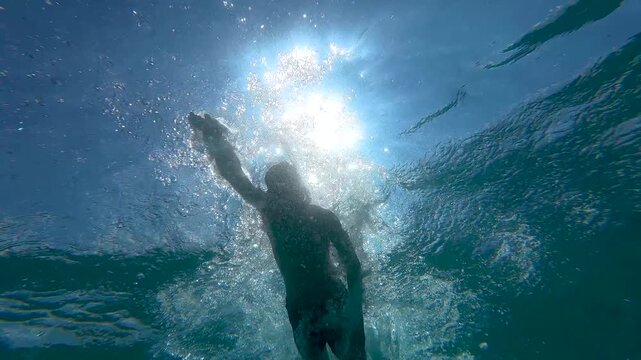 Teenage boy swims and dives underwater in the ocean wearing a diving mask during an active outdoor summer experience.