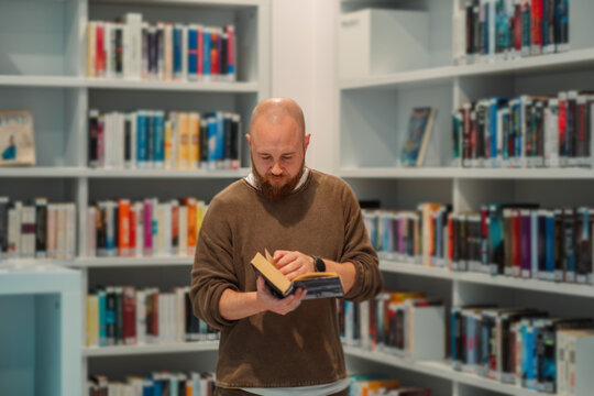 Man standing and reading in the middle of a library hall