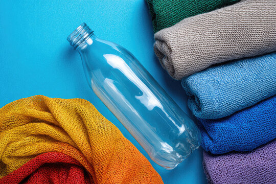 Plastic recycling and reuse concept. Empty plastic bottle and various fabrics made of recycled polyester fiber synthetic fabric on a blue background. Environmental protection waste recycling.