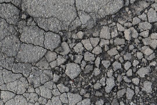 A mosaic of decay: asphalt fragments break apart like tectonic plates, revealing the raw, dusty impermanence of a once-smooth surface in a play of deep light and shadow.