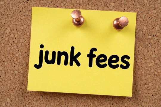 Yellow sticky note with junk fees text pinned on corkboard. This message serves as a reminder about unnecessary extra charges, potential scams, and financial problems.
