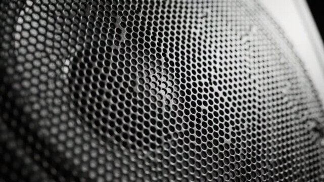 Macro close up of speaker grill with vibrating audio membrane pulsating inside black mesh casing showing sound frequency motion and dynamic acoustic patterns.
