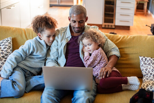 Father and two children watching laptop on sofa at home