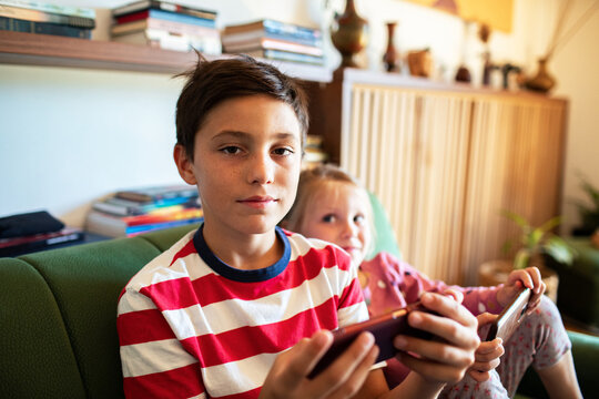 Siblings playing mobile games on couch at home