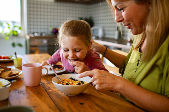 Mother and daughter eating breakfast cereal in home kitchen