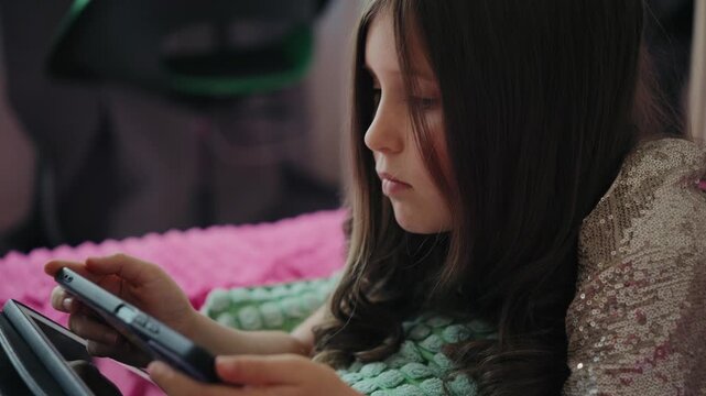 Focused Caucasian girl lying in bed at home and playing a video game on her smartphone.