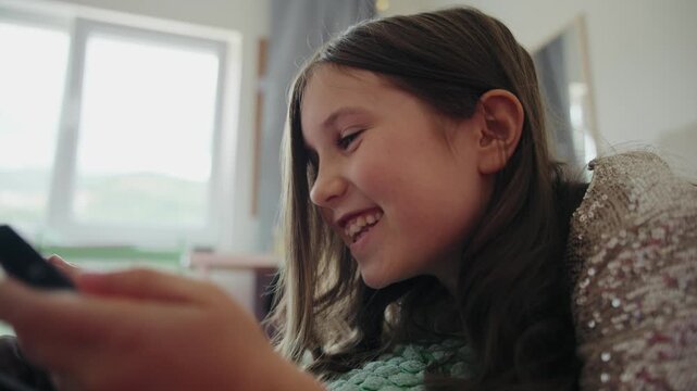 Happy girl lying down at home and excitedly playing mobile games on a smartphone.