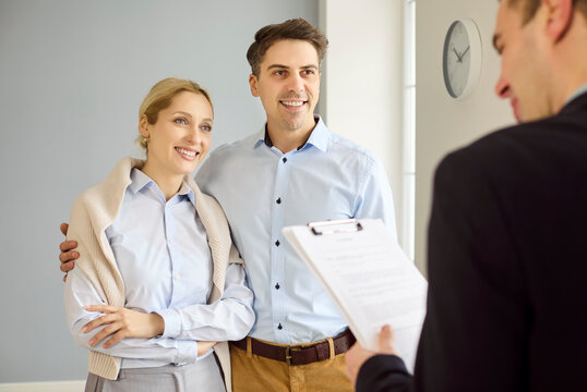 Couple and realtor review property contract. Client couple stand in an apartment as the agent details home buy options and prepares documents for signature. Concept shows real estate showing.
