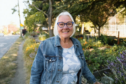 Candid smiling senior woman outdoors in denim jacket and glasses