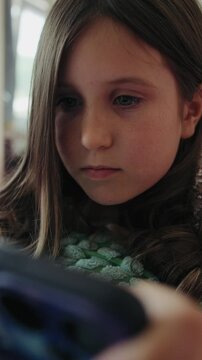 Vertical video of a focused young girl looking at a smartphone screen at home.