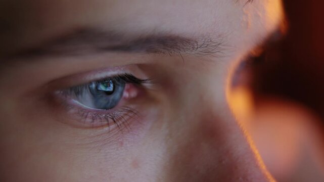 Extreme close-up of a teenage boy's blue eye reflecting a computer screen in a dark room.