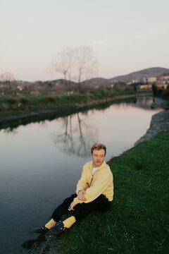 Person sitting by a river at sunset in a green area