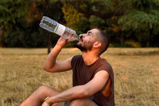 Young Man Drinking Water While Resting Outdoors on a Summer Evening