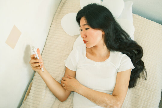 Overhead of relaxed young asian woman using smartphone lying in bed