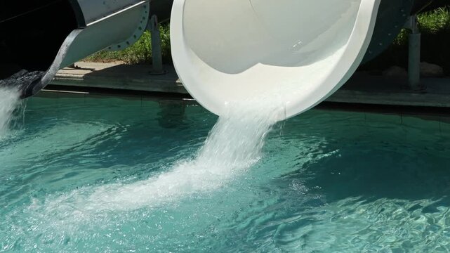 Close-up view of water flowing from waterslide exits into swimming pool in slow motion. Greece. 