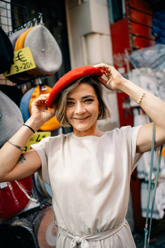 Woman Tries on Red Beret in Market Stall With Various Hats