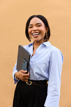 Happy hispanic woman holding tablet standing in front of orange wall