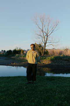 Person stands near water with trees and clear sky in background