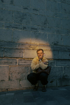 Person sitting against a stone wall in a quiet area during evening
