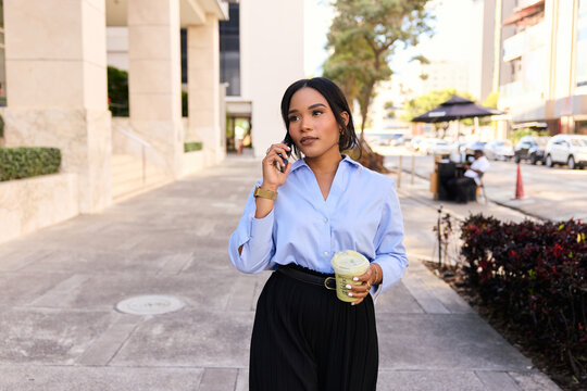 Hispanic Woman Talking on phone While Walking on City Street