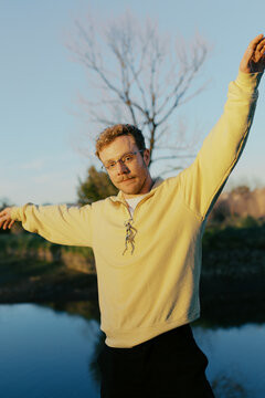 Person poses with arms outstretched by a body of water in nature