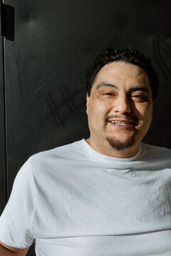 Candid portrait of a smiling man in white shirt against dark wal