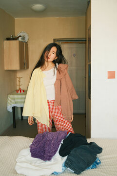Young emotional asian woman choosing what clothes to wear 