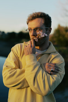 Young man poses with flowers near water at sunset