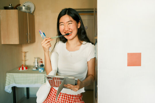 Young happy asian woman holding a tablet and brushing teeth 