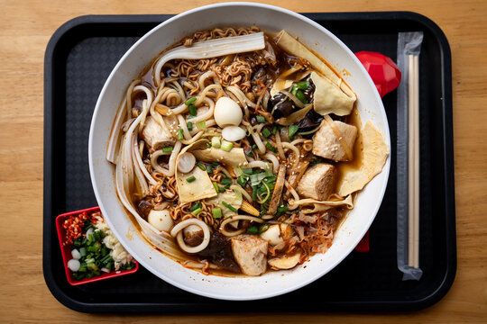 A big bowl of spicy vegetarian mala noodle soup on a tray 