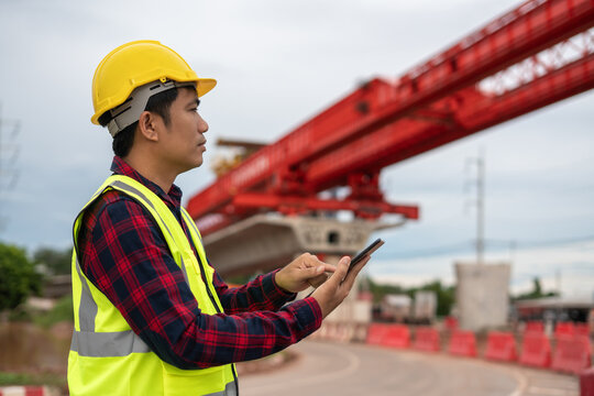 Construction worker wearing a yellow hard hat and reflective safety vest using a smartphone at a construction site