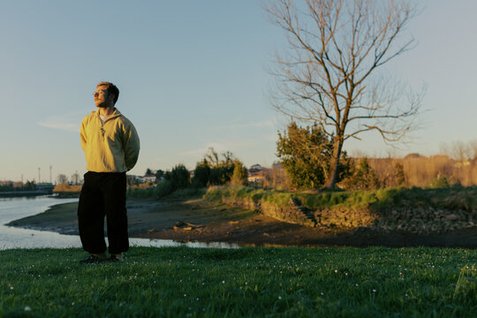 Person stands by riverbank during late afternoon