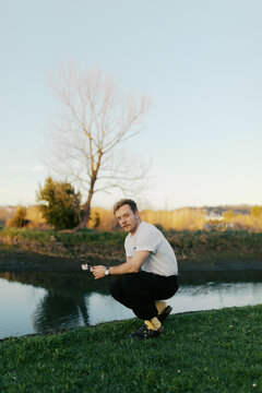 Man squatting by a river at sunset holding a flower