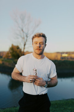 Man stands by water holding flower in hand during sunset