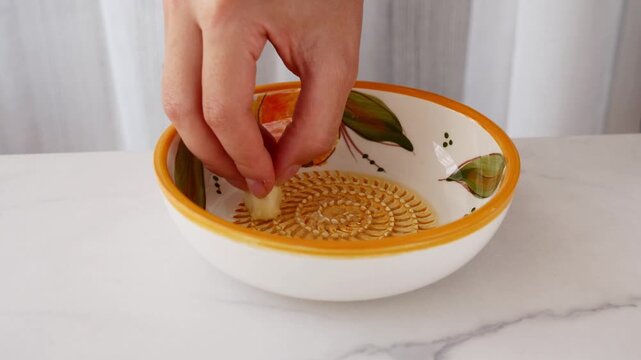 Close-up of woman grating fresh garlic on traditional Spanish ceramic grater plate. Authentic Mediterranean cooking and food preparation.