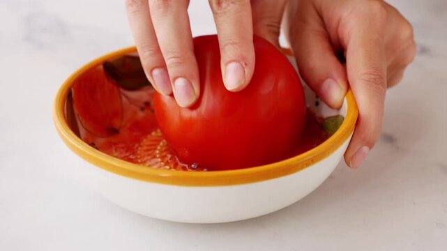 Close-up of woman hands grating fresh tomato on traditional Spanish ceramic grater plate. Preparing natural tomato pulp for pan con tomate, authentic Spanish and Mediterranean cuisine.