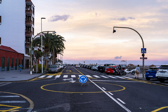 Santa Cruz de La Palma, Spain - 01 January 2026: View of a coastal road at sunset with a temporary roundabout sign, parked cars, palm trees, and pedestrians along the promenade.