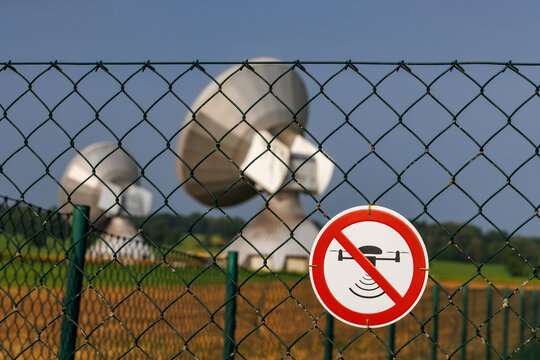 No drone zone sign attached to wire fence in front of large satellite dishes, drone flight restriction and security area concept