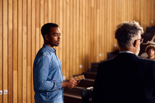 An assistant stands beside a professor in a lecture room