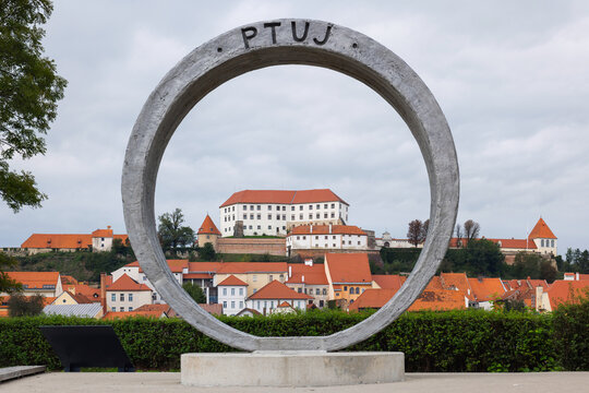 People explore the town of Ptuj while looking at the castle and the unique ring sculpture. The Drava River flows nearby.