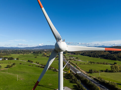 A wind turbine stands tall in a green area, producing clean energy under a clear sky with distant mountains in view.