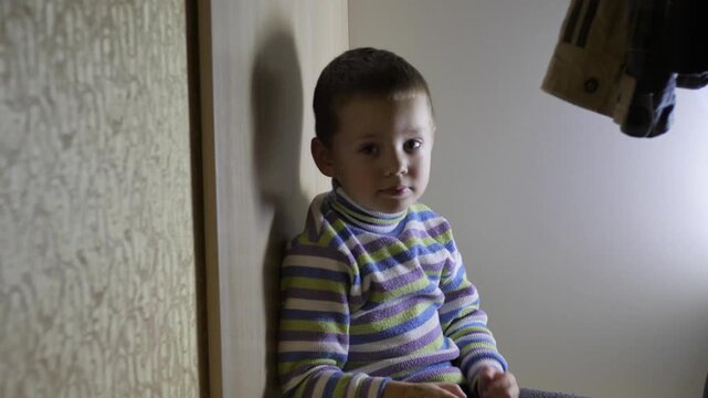 a little boy is sitting in the closet and telling something