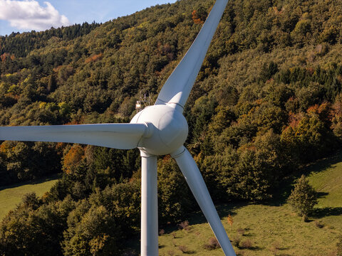 A wind turbine is visible on a hillside among trees and grass. The location shows the use of renewable energy sources.