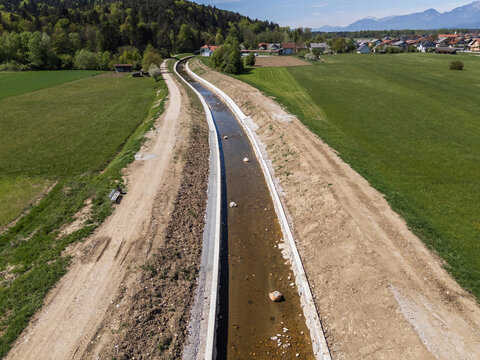 Aerial view of a river restoration site featuring channel cleaning and flood prevention efforts in a rural area under clear skies.