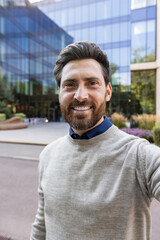 Fototapeta premium Vertical close-up photo of a young man standing outside a building, holding a camera in his hand and chatting online