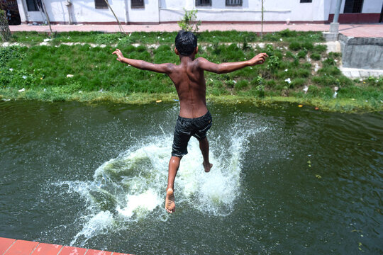 Narayanganj, Dhaka, Bangladesh - 17 April 2019: View of a young boy jumping into a canal with a large splash, surrounded by grassy banks and urban buildings.